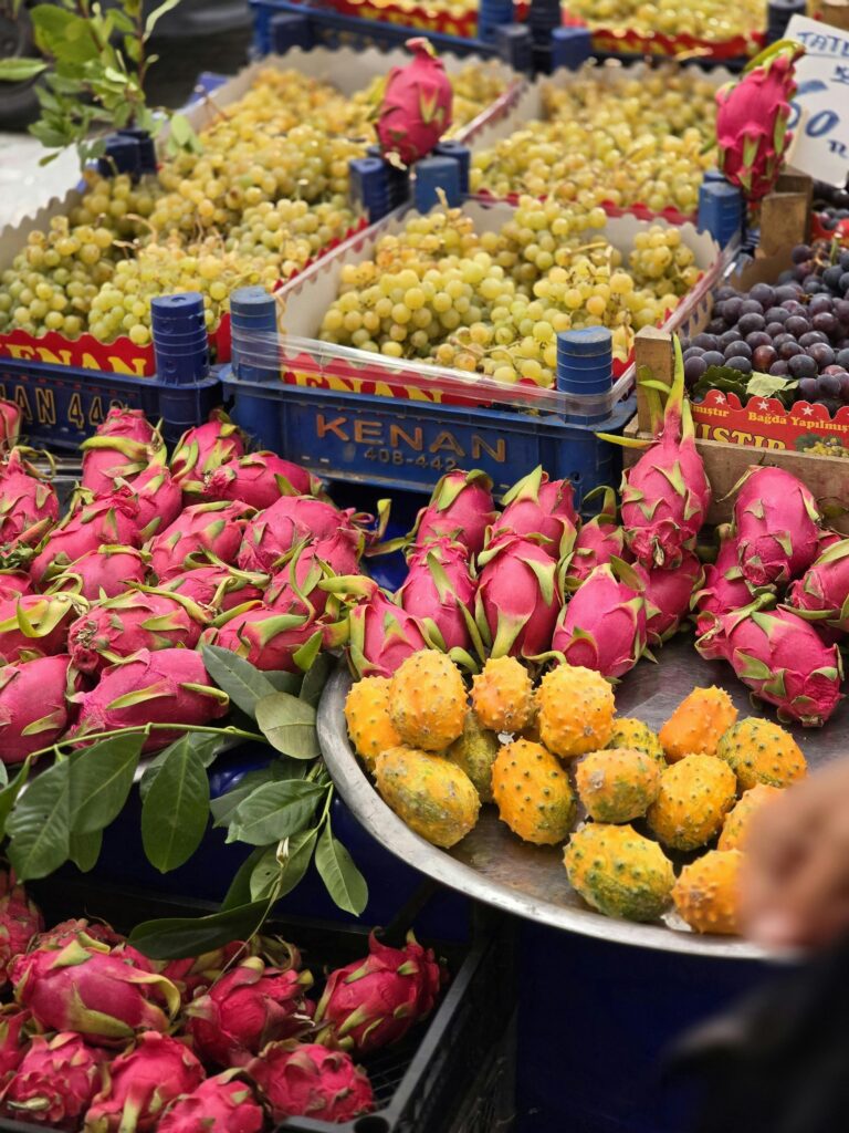 Vibrant display of dragon fruit, kiwano, and grapes at an outdoor market stall.